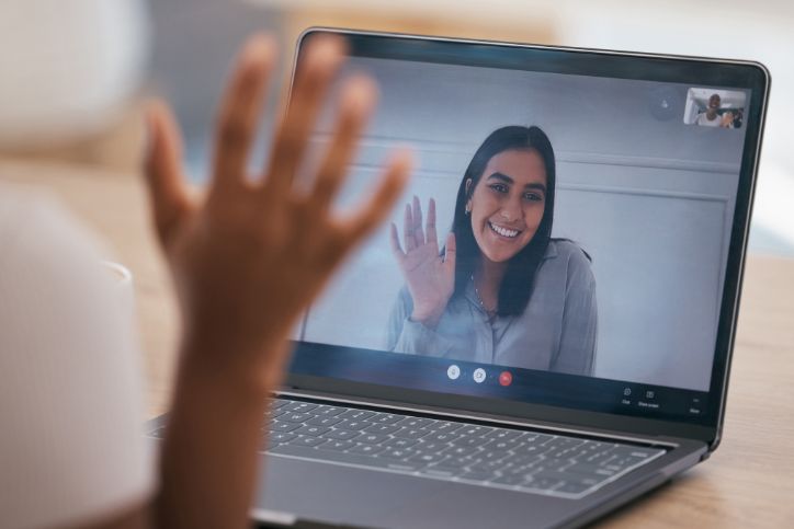 A woman's hand is waving at another woman on the computer screen